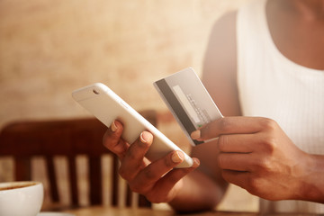 Cropped portrait of African American housewife wearing casual top, using mobile phone, entering information on her credit card while signing up on food delivery website while spending evening at home