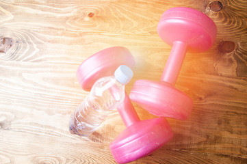 Two pink dumbbells and water. Fitness concept for women