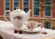 Чай в изящном сервизе, чайный пакет и ягоды вишни  на балконе на фоне окон.