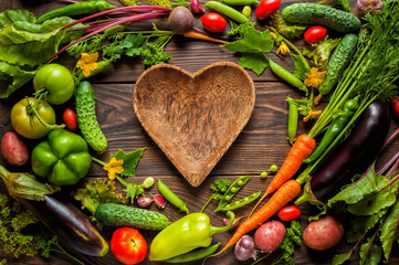 Plate heart shape surrounded with Fresh organic Vegetables on Wooden Background. Healthy Vegetarian food, View from above.