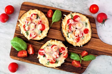 Wall Mural - Healthy eggplant mini pizzas with melted mozzarella, tomatoes and basil on a serving board against marble