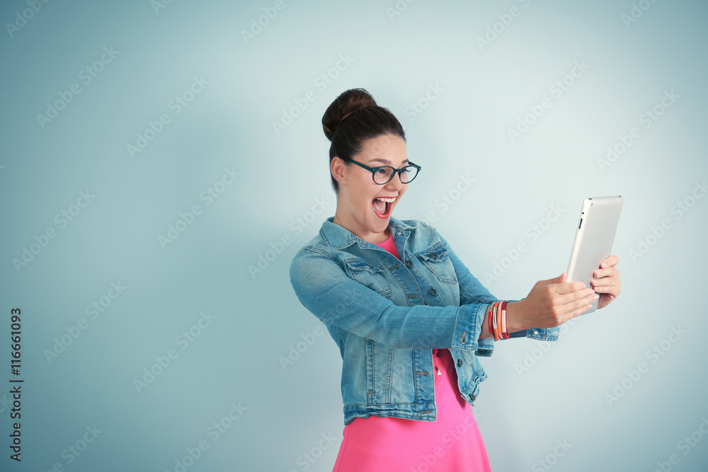 Cute young woman holding tablet on light background