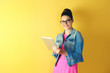 Cute young woman holding tablet on yellow background