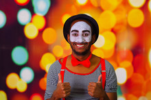 Pantomime Man With Facial Paint Posing For Camera Interacting Giving Thumbs Up Smiling, Blurry Lights Background