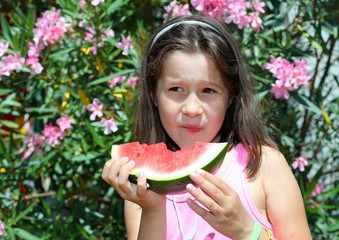 little girl with brown hair eating a slice of watermelon in summ