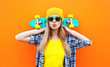 Fashion pretty cool girl with skateboard over colorful orange ba