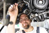Fototapeta Przeznaczenie - freundlicher Automechaniker repariert Motor eines Fahrzeuges in der Werkstatt // friendly car mechanic repairs engine of a vehicle in the garage