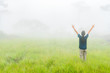 © chanwitohm - Happy young woman rising hand and enjoying misty day on green morning