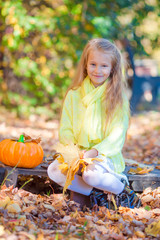 Wall Mural - Adorable little girl with a pumpkin for Halloween outdoors at beautiful autumn day