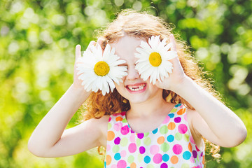 Child with daisy on green bokeh background in a summer park.