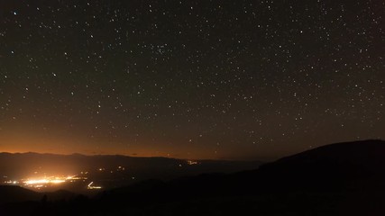 Wall Mural - Time Lapse of the stars moving across the night sky. Mountain and the lights from a small town can be seen at the bottom of the screen.