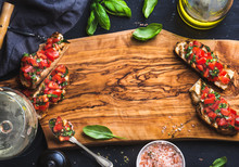 Tomato And Basil Bruschetta With Glass Of White Wine On Olive Wooden Board Over Black Background, Top View, Copy Space, Horizontal Composition