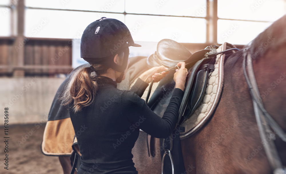 Woman rider adjusting her stirrups on her saddle - obrazy, fototapety, plakaty 