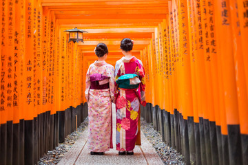 two geishas among red wooden tori gate at fushimi inari shrine in kyoto, japan. selective focus on w