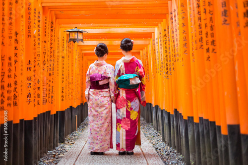Fotografía Two geishas among red wooden Tori Gate at Fushimi Inari Shrine in Kyoto, Japan