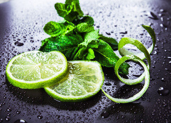 Green limes with mint and water drops on black background