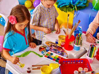 Two children girl and boy with brush painting on table in primary school. Painting children lesson in primary school. Small table in painting class.