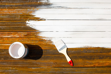 painting with white paint rusty metal surfaces. bucket with white paint and a paint brush on a rusty metal surface. part of the metal painted white. top view