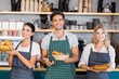 © WavebreakmediaMicro - Smiling waiter and two waitresses holding plate of bread rolls