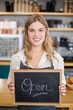 © WavebreakmediaMicro - Smiling waitress showing chalkboard with open sign at cafe