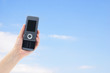 © ImagePixel - Hand holding a cell phone a blue sky background.