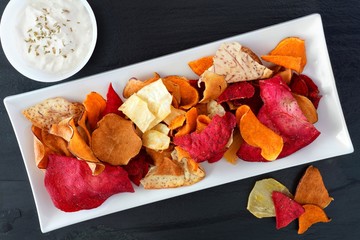 Plate of colorful healthy vegetable chips with dip, above view on a slate background