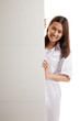 © halfbottle - Young Asian female doctor peeking from behind blank sign billboa