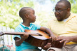 © digitalskillet1 - African American man teaching his son how to play the guitar
