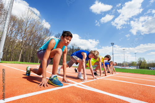 Fototapeta Five teenage athletes ready to run on a racetrack