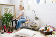 © Mint Images - A young woman sitting on a chair in an apartment decorated with pictures and plants.