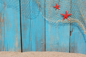 Fishing net and red starfishes against an old blue wooden backgr