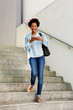 © mimagephotos - Smiling woman with mobile phone walking down the steps