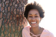 © mimagephotos - Beautiful young african woman leaning on tree