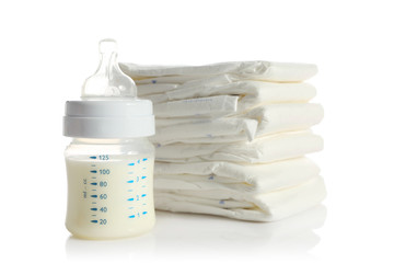 Fototapete - Baby bottle with milk and pile of diapers isolated on white
