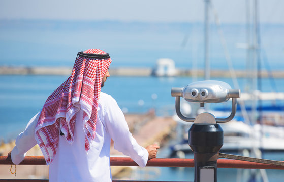 Arabian man looking at the yacht harbor, back view