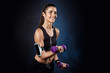 Young beautiful sportive girl training with dumbbells over dark background.
