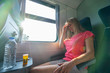 Headache and motion sickness. Stressed and tired young woman sitting near the window and with bottle of water and tablets on table while travelling by train.