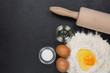 Ein Hügel Mehl mit einem aufgeschlagenen Ei in der Mitte. Daneben eine Schale Öl, Salz und Eier. Eine Teigrolle als Werkzeug auf einer Schieferplatte.