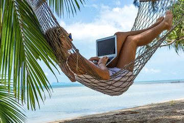 Poster - Young woman with a laptop in a hammock on the beach
