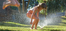 Young Girls Playing Jumping In A Garden Water Lawn Sprinkler