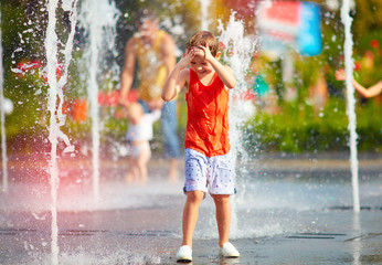 excited boy having fun between water jets, in fountain. Summer in the city