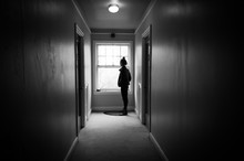 Young Woman In A Dark Hallway Looking Out A Window.
