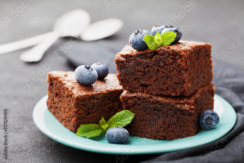 Zdjęcie XXL Pączek Brownie ozdobiony jagodami i listkami mięty. Czekoladowy tort w turkusu talerzu na rocznika czerni stole. Domowe ciasto na deser.