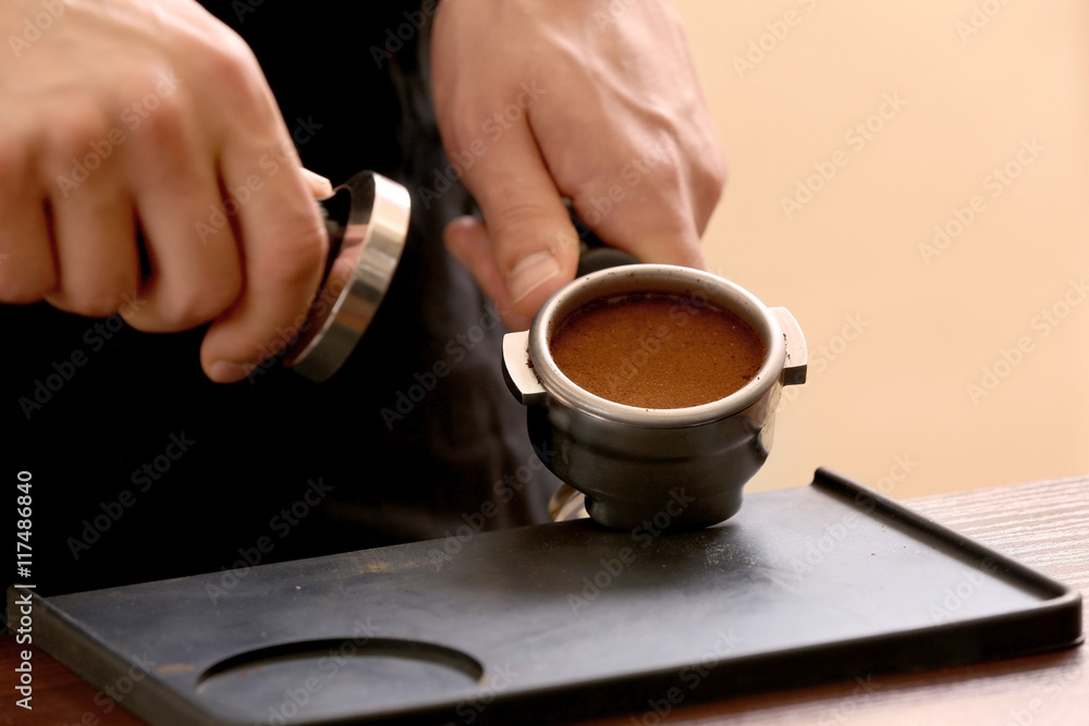 Barista pressing ground coffee with tamper in portafilter