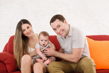 Happy mother and father plays with son on the red sofa