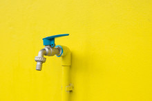 Closeup Faucet On Concrete Yellow Wall Background. Water Leaking