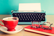 Turquoise Typewriter, Coffee Cup And Eyeglasses Over Red Notebook
