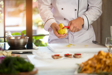 Wall Mural - Man's hand peeling a pear. Chef near white cooking board. Sweet ingredient for sauce. Need fresh fruit.