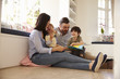 © Monkey Business - Family Sitting On Floor Reading Story At Home Together