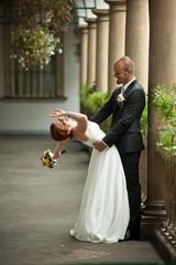 Wall Mural - Bald-headed groom bends bride over standing on the balcony